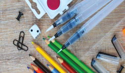 Art supplies on a desk: paints, paperclips, colored pencils and dice