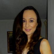 A woman with long, curly brown hair looking directly at the camera and smiling
