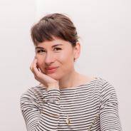 Portrait of a smiling adult with fashionable bangs and a striped shirt, sitting in front of a book on a table