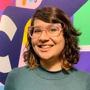 Photo portrait of a smiling young adult with pink glasses, wavy hair and a colorful background