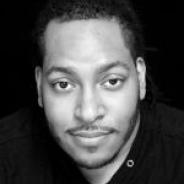 Black and white photo of Jerrod looking into camera on a stark black background.