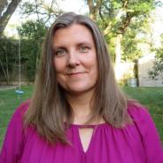 photo of a white woman with light brown hair. She is standing outside and wearing a bright pink shirt.