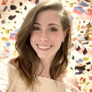 A white woman with shoulder-length brown hair smiles with colorful paint in the background.