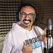 An Ecuadorian man wearing headphones and glasses standing in front of a microphone. Juan Carlos has a mustache and goatee. He is smiling at the camera and giving a thumbs up sign.