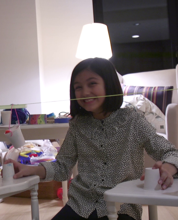 An adult and a child work on an engineering design project together using cups and string